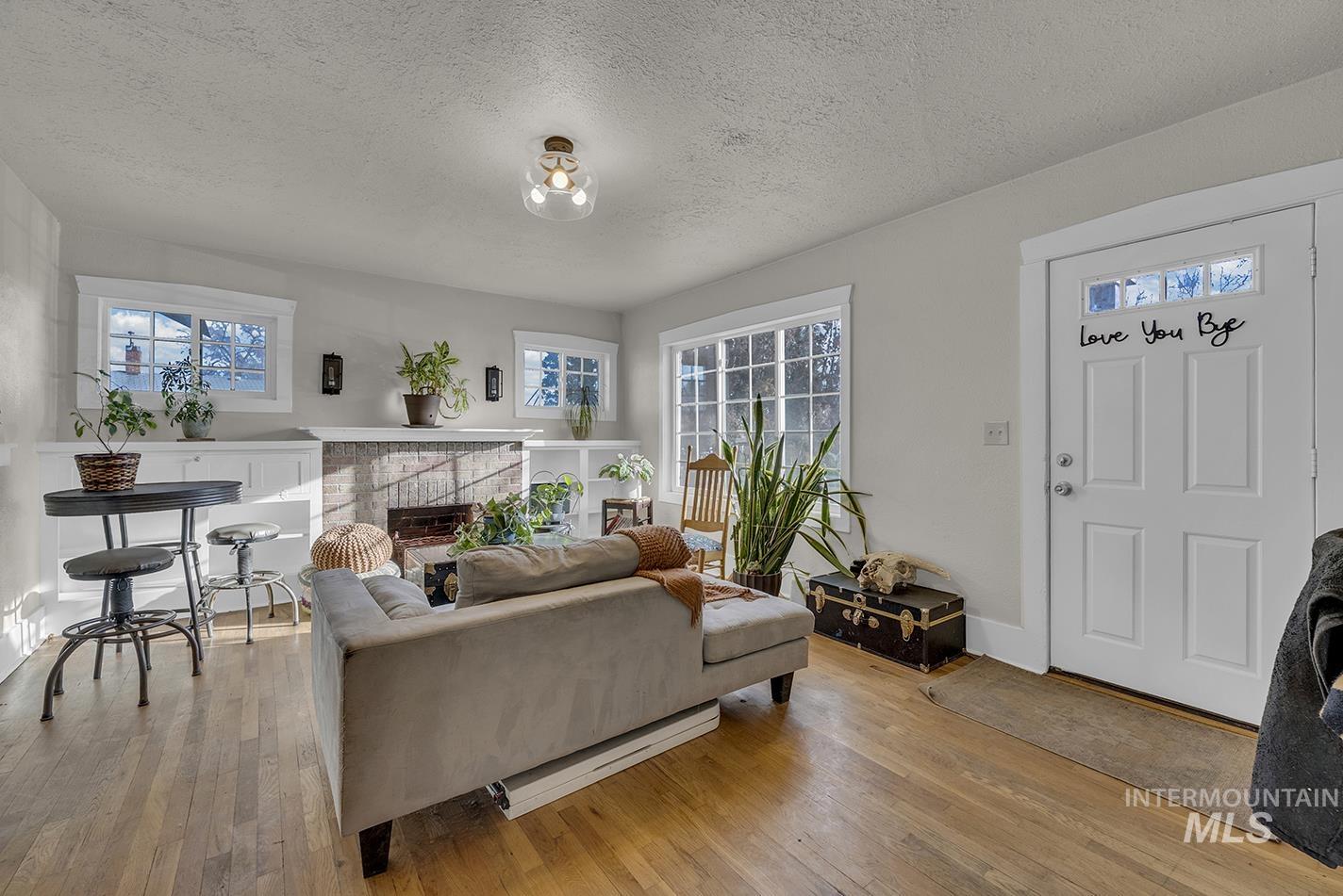 Living room featuring a textured ceiling, a brick fireplace, and light wood finished floors