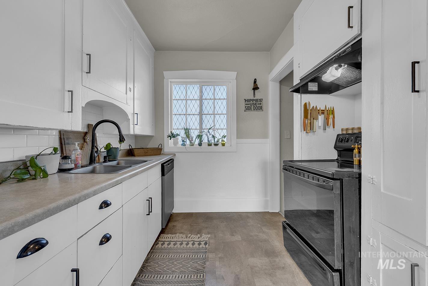 Kitchen with black / electric stove, white cabinets, exhaust hood, and light countertops