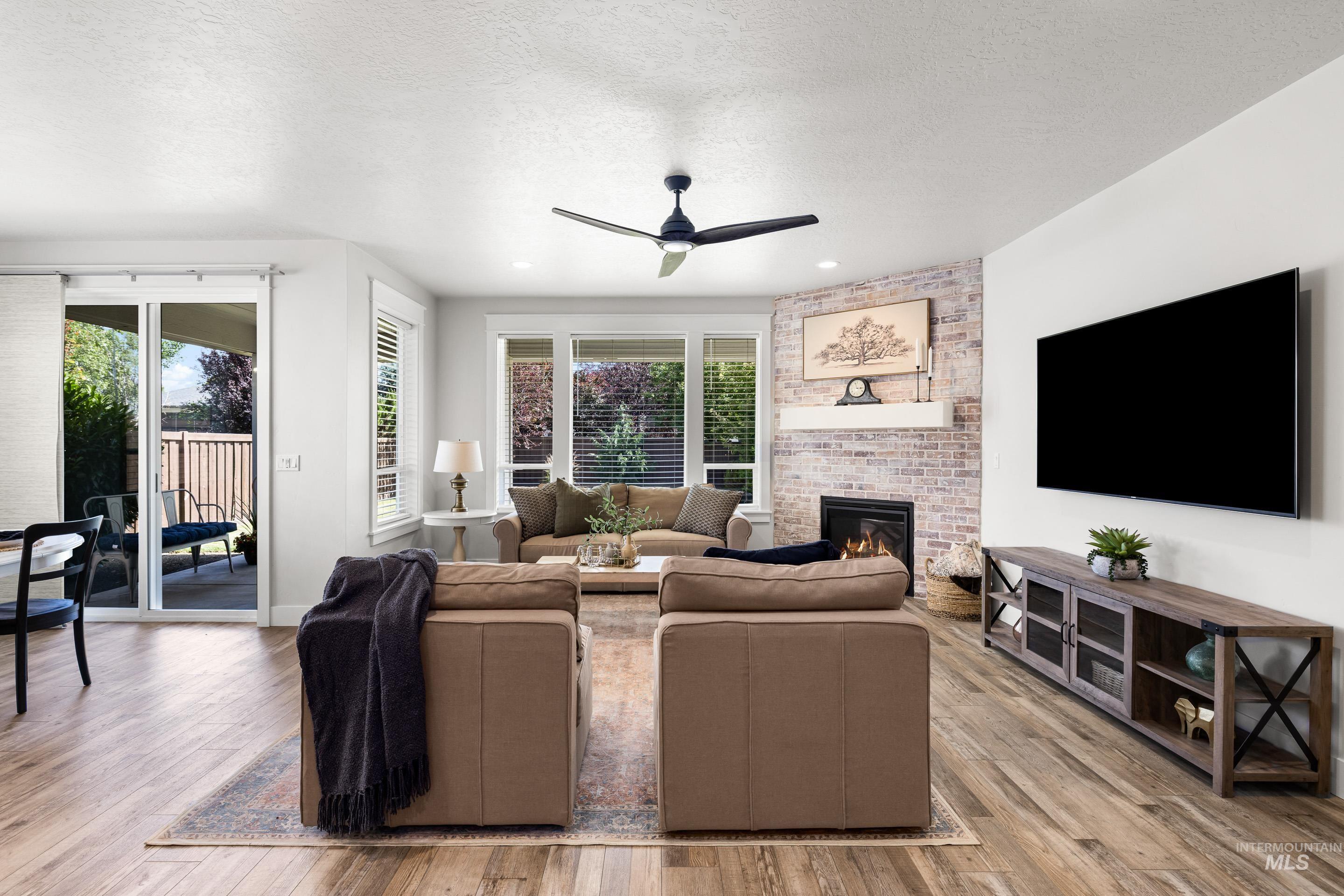 Living area with ceiling fan, healthy amount of natural light, a fireplace, wood finished floors, and a textured ceiling