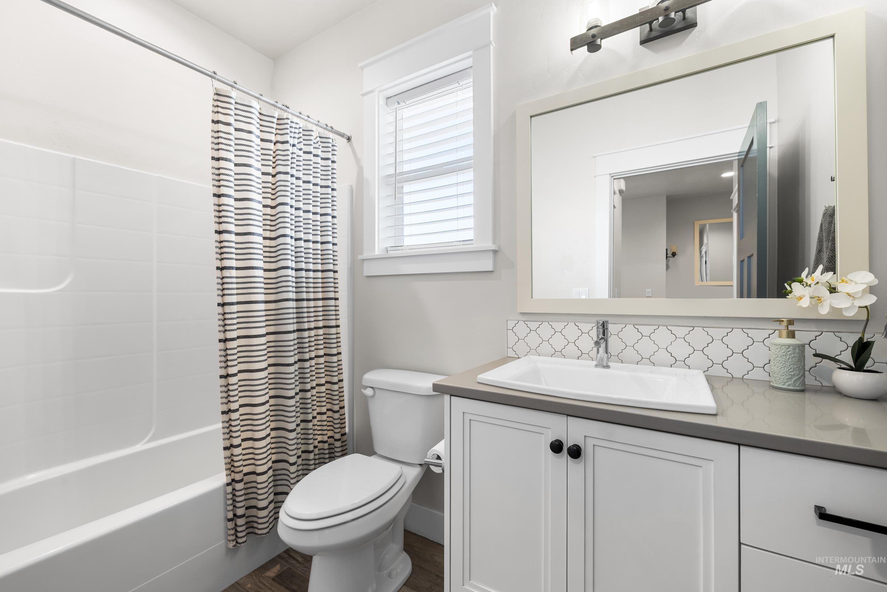 Full bathroom with vanity, backsplash, shower / tub combo with curtain, and wood finished floors