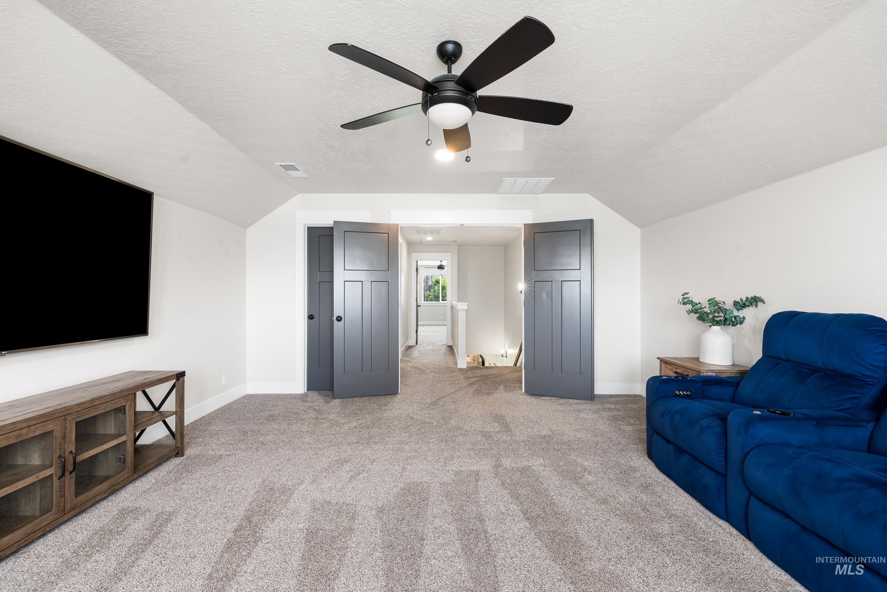Living area featuring a ceiling fan, lofted ceiling, light carpet, and a textured ceiling