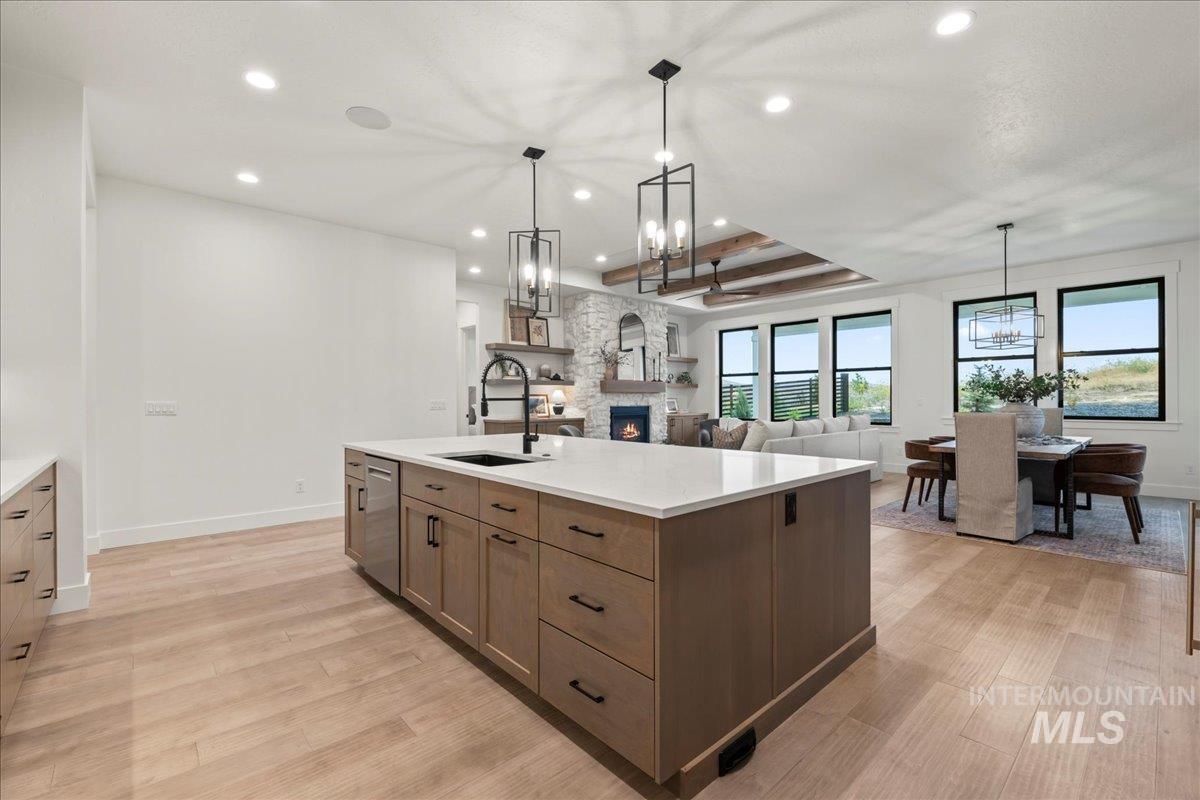 Kitchen featuring a chandelier, a raised ceiling, a fireplace, open floor plan, and a kitchen island with sink