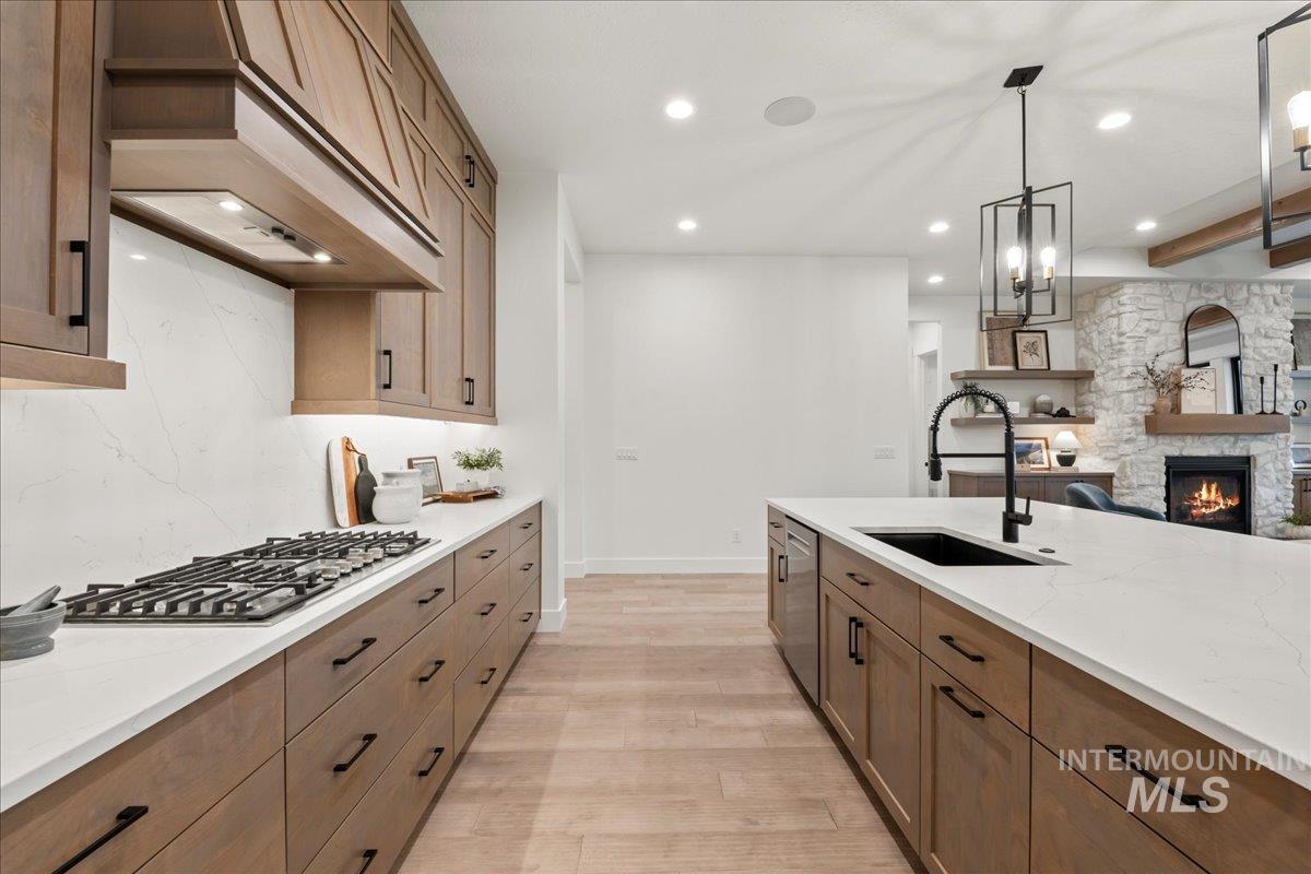 Kitchen featuring brown cabinetry, light stone countertops, pendant lighting, open floor plan, and light wood finished floors
