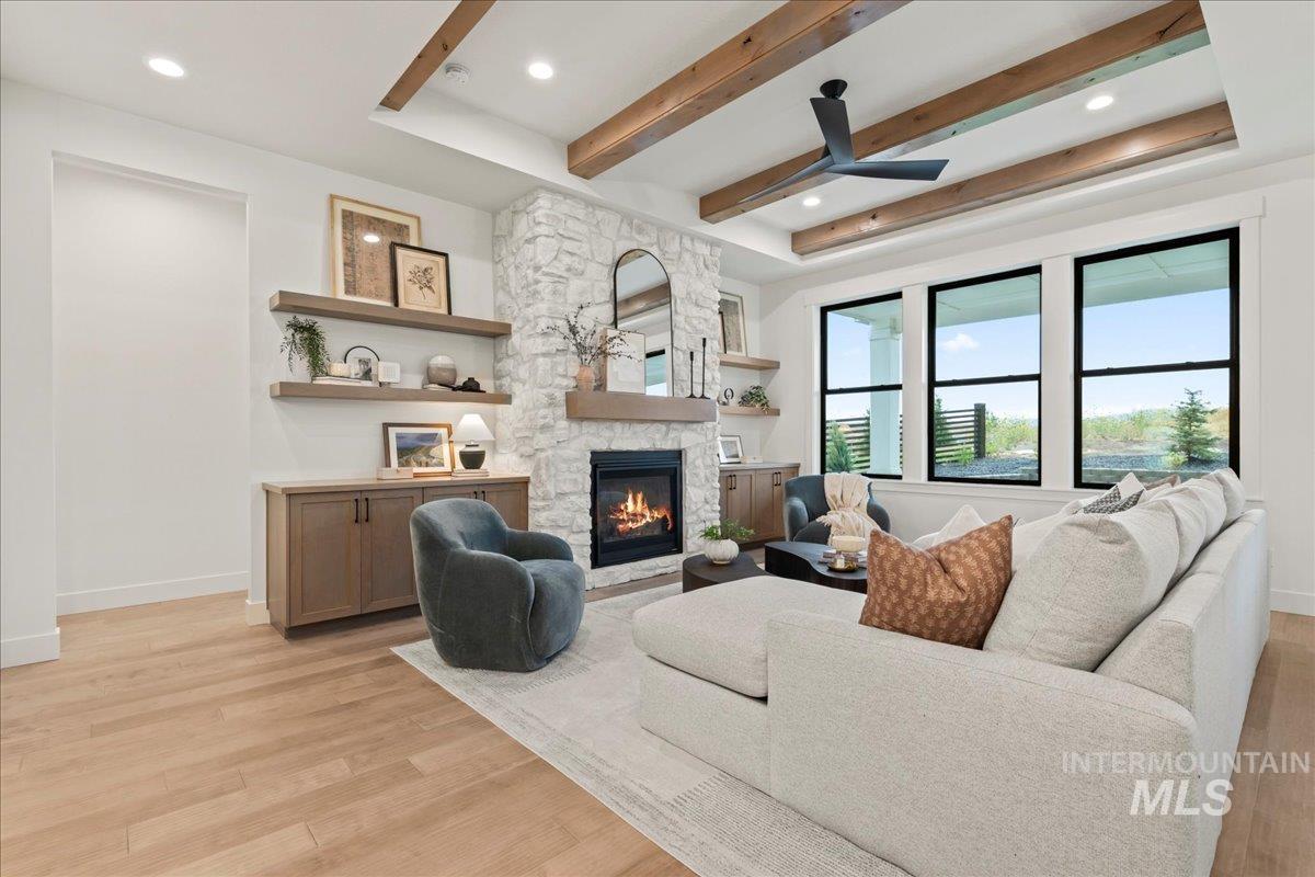 Living area with beamed ceiling, a stone fireplace, light wood-style floors, ceiling fan, and recessed lighting