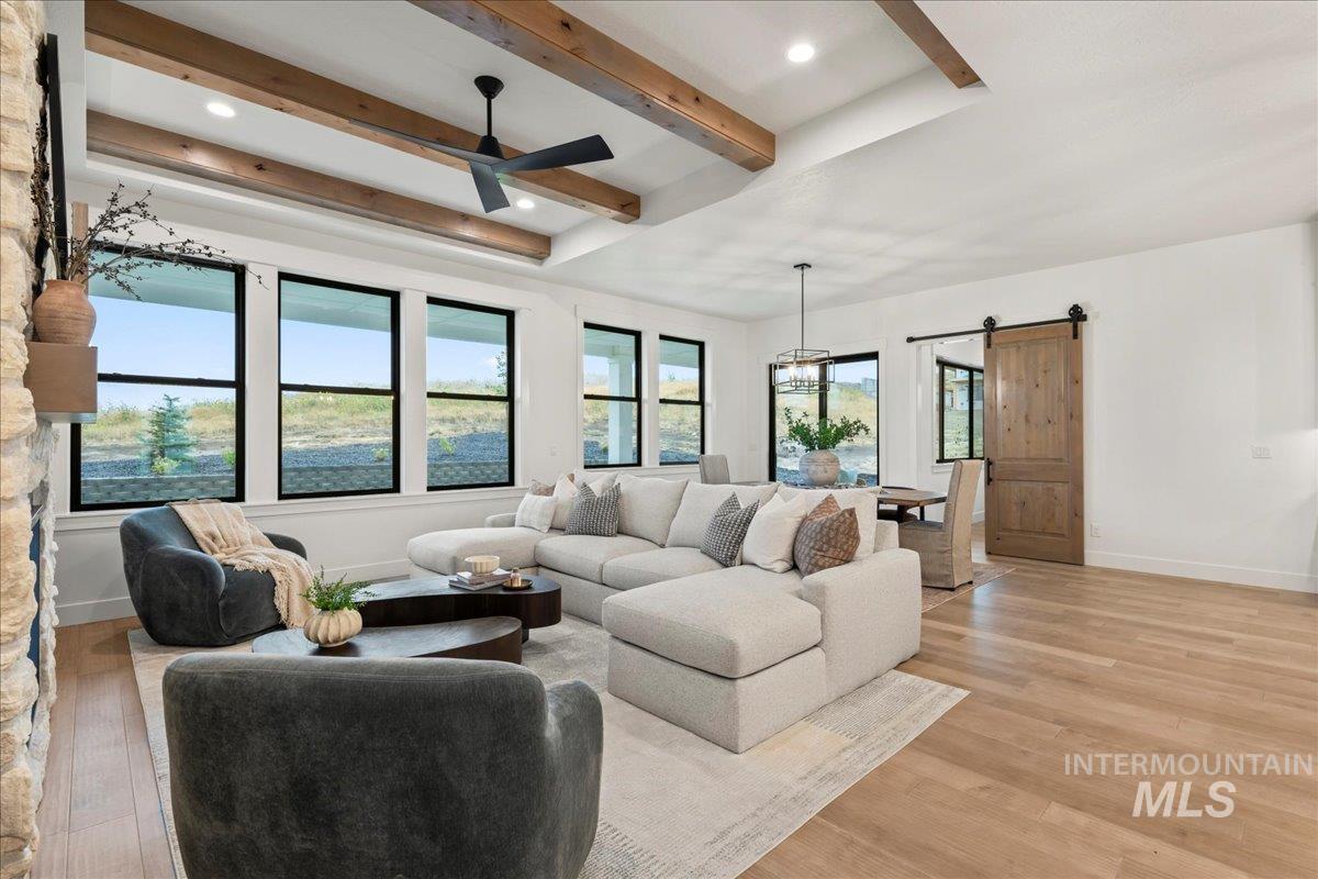 Living room featuring a barn door, beam ceiling, light wood-style flooring, recessed lighting, and ceiling fan