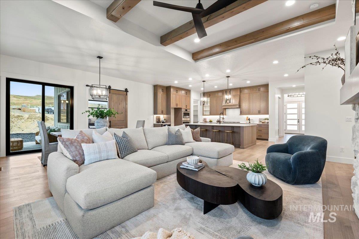 Living area featuring beam ceiling, light wood-type flooring, a barn door, recessed lighting, and a chandelier