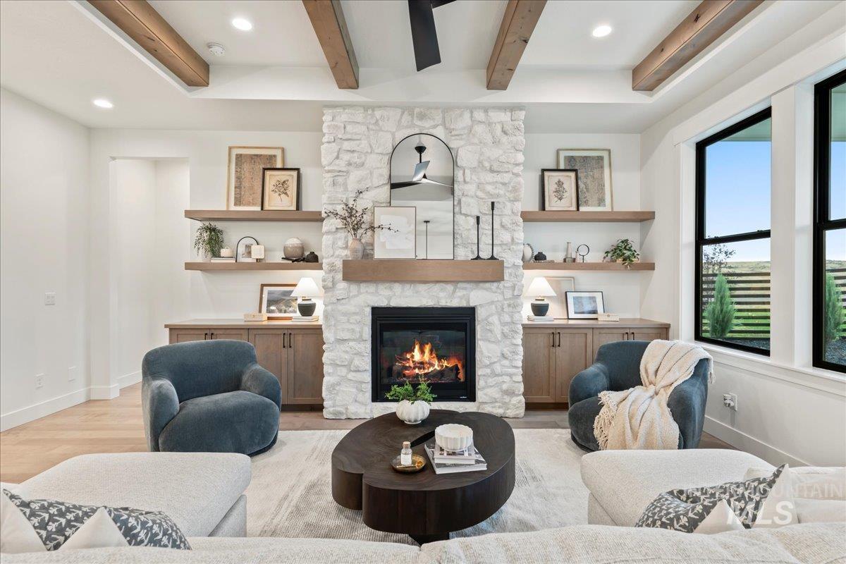 Living area with a stone fireplace, beam ceiling, light wood-style floors, and recessed lighting