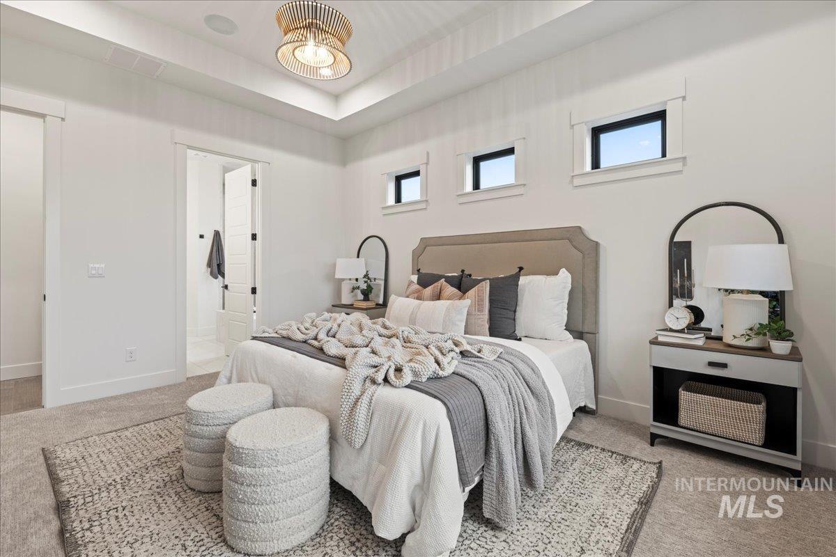 Bedroom with light carpet, multiple windows, a tray ceiling, and ensuite bath