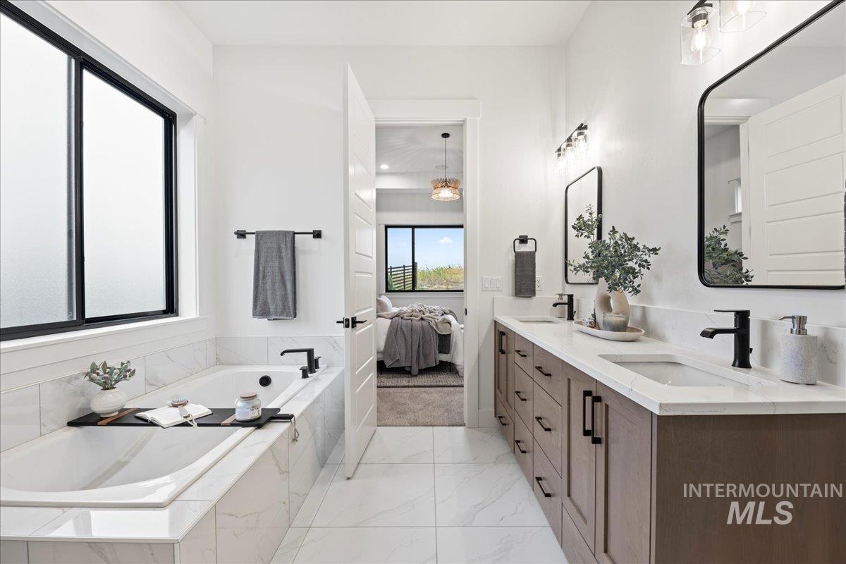 Bathroom featuring a bath, double vanity, connected bathroom, and light marble finish floors