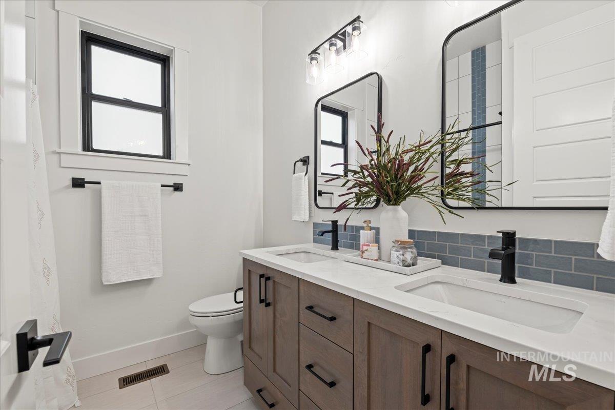 Full bathroom featuring double vanity, light tile patterned flooring, and backsplash