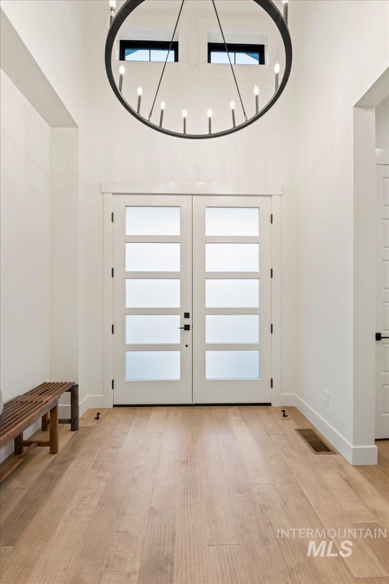 Foyer with french doors, a high ceiling, light wood-style floors, and a chandelier