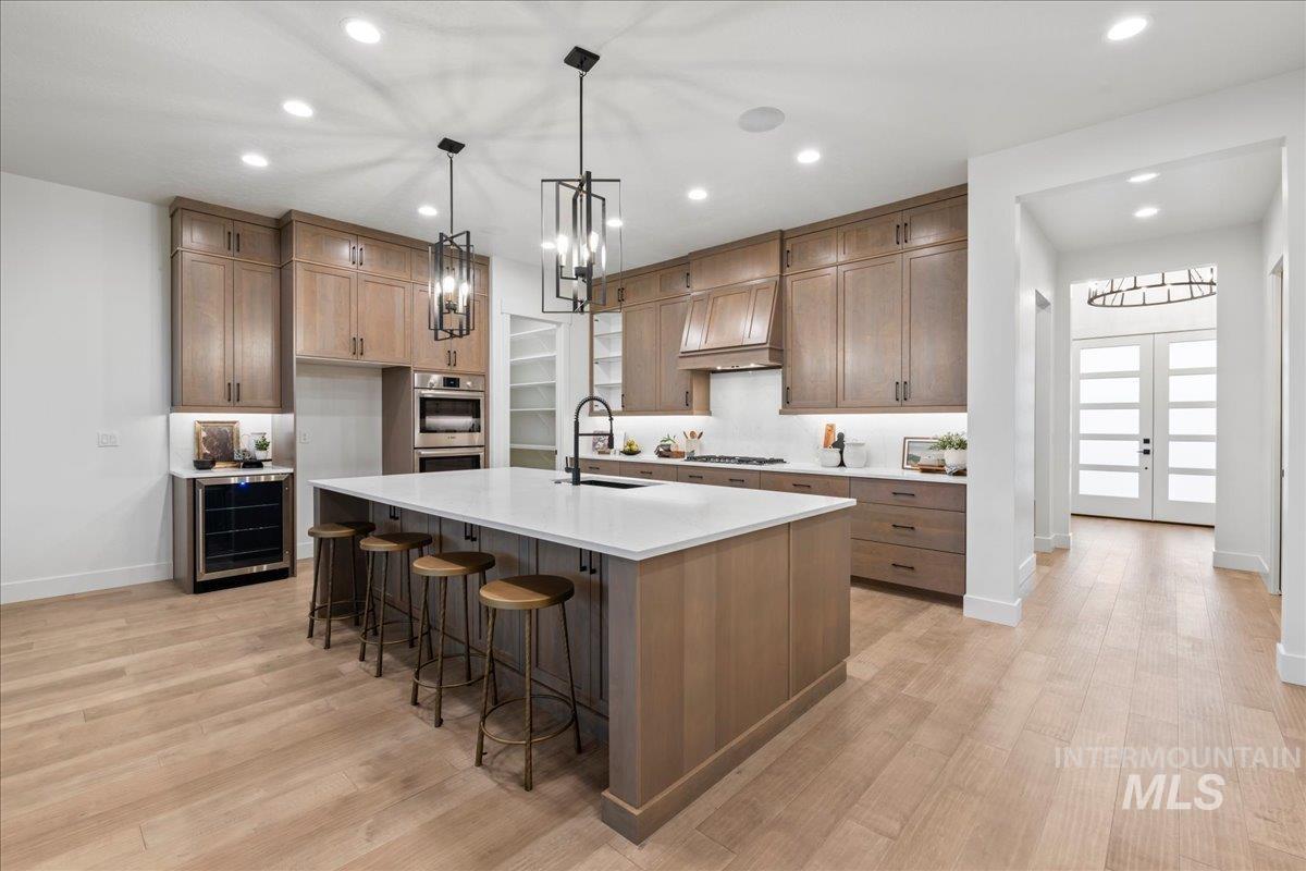 Kitchen with decorative light fixtures, recessed lighting, a kitchen breakfast bar, brown cabinetry, and light stone counters