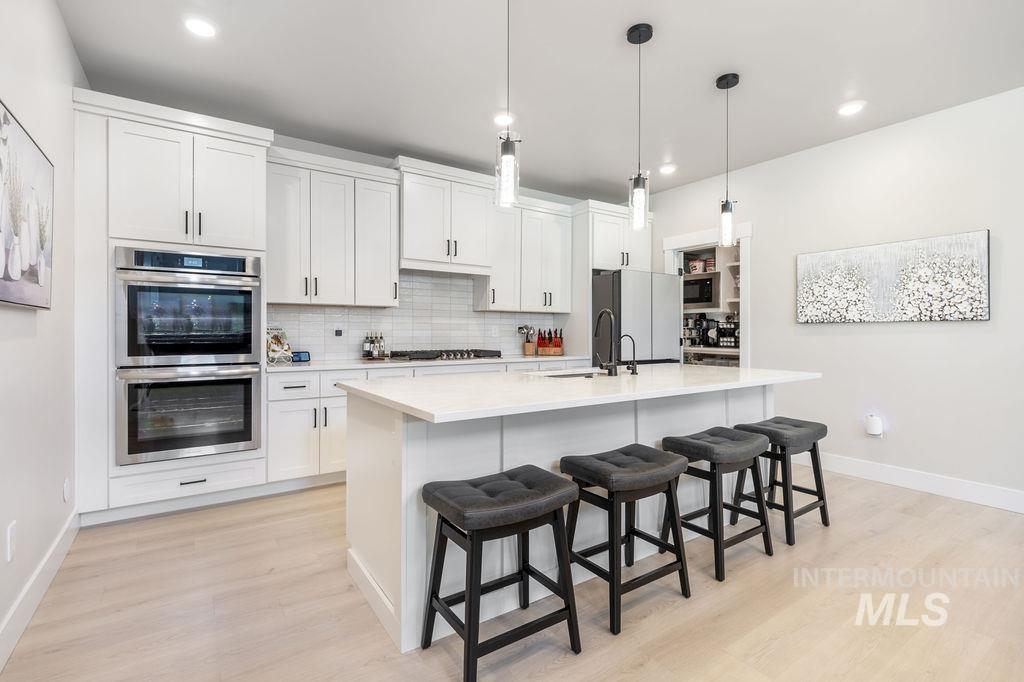 Kitchen featuring appliances with stainless steel finishes, tasteful backsplash, a breakfast bar area, decorative light fixtures, and white cabinets