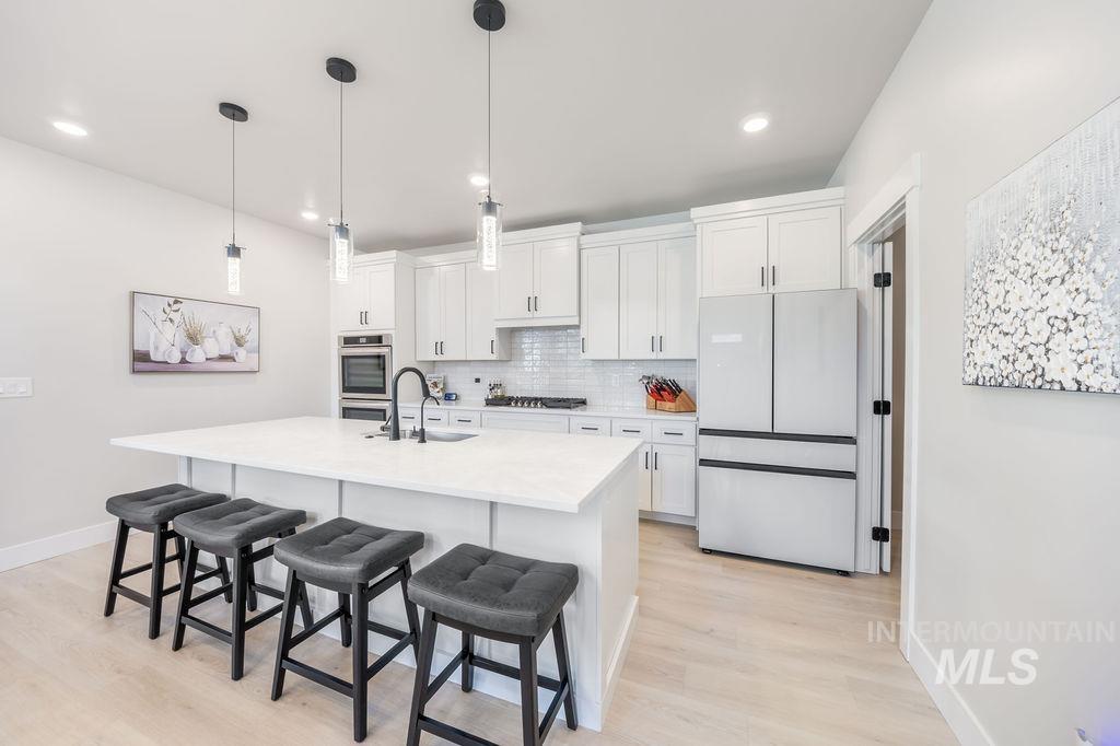 Kitchen with backsplash, a breakfast bar area, appliances with stainless steel finishes, hanging light fixtures, and white cabinetry