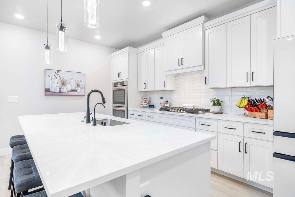 Kitchen with a breakfast bar area, white cabinets, decorative light fixtures, appliances with stainless steel finishes, and a kitchen island with sink