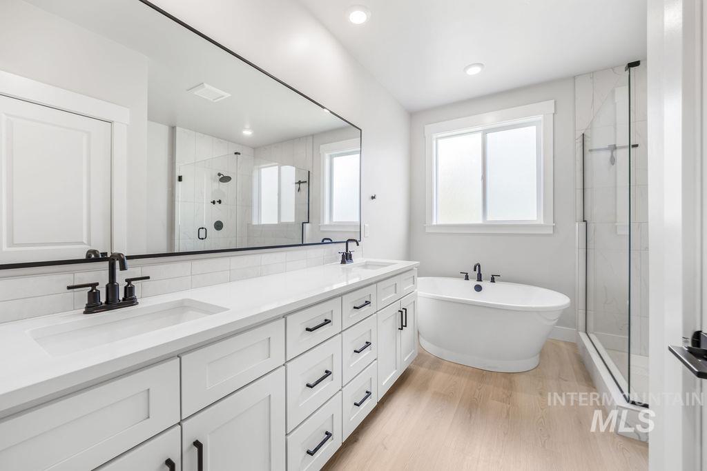 Full bath featuring a stall shower, double vanity, a freestanding bath, light wood-type flooring, and recessed lighting