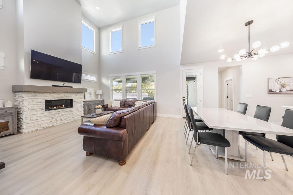 Living area with light wood-style floors, a high ceiling, a chandelier, a stone fireplace, and recessed lighting