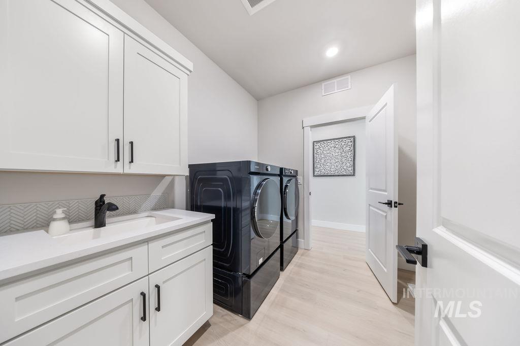 Laundry area featuring light wood finished floors, cabinet space, washing machine and clothes dryer, and recessed lighting
