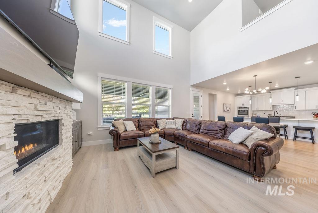 Living room with light wood-style floors, a chandelier, a stone fireplace, a high ceiling, and recessed lighting