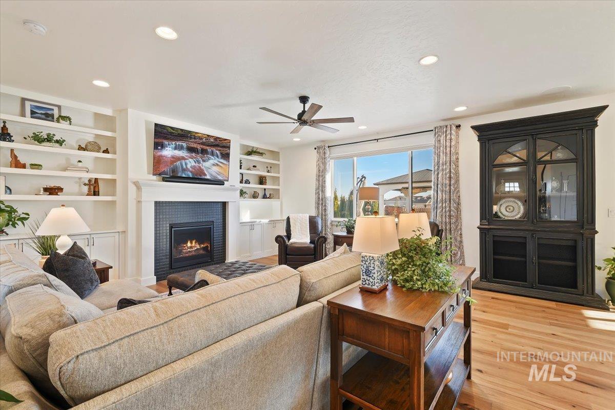 Living room featuring built in shelves, light wood-style flooring, a fireplace, recessed lighting, and a ceiling fan