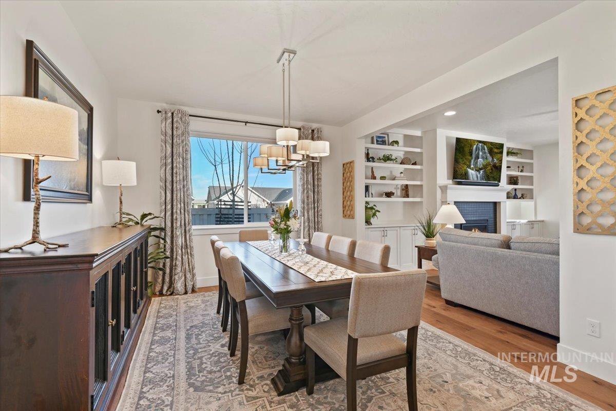 Dining area with a lit fireplace, built in shelves, light wood finished floors, recessed lighting, and a chandelier