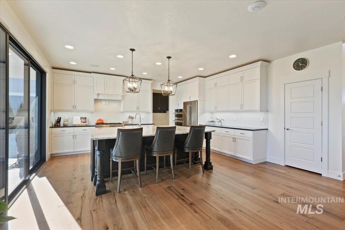 Kitchen with hanging light fixtures, white cabinets, a center island with sink, a kitchen breakfast bar, and appliances with stainless steel finishes
