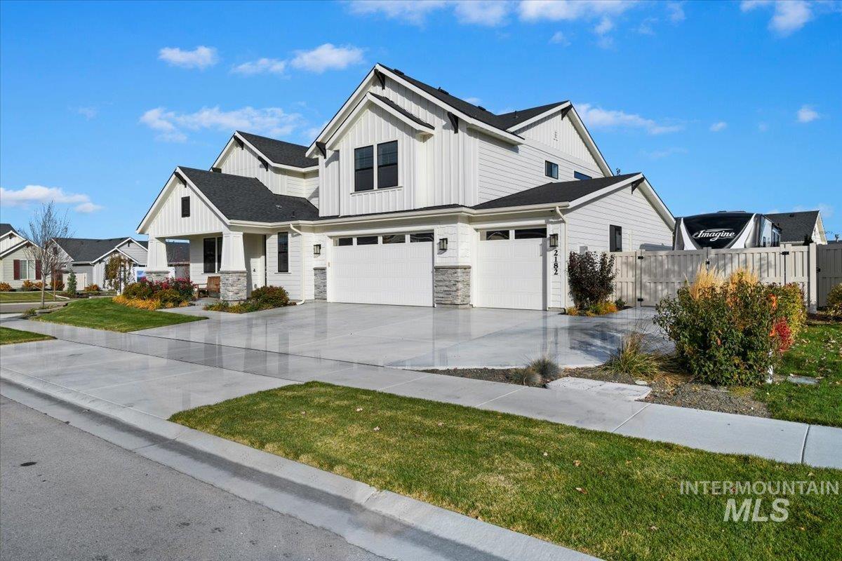 Modern farmhouse with board and batten siding, an attached garage, driveway, and stone siding
