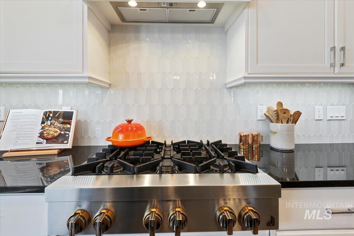 Kitchen view of dark stone countertops, white cabinetry, decorative backsplash, and range hood