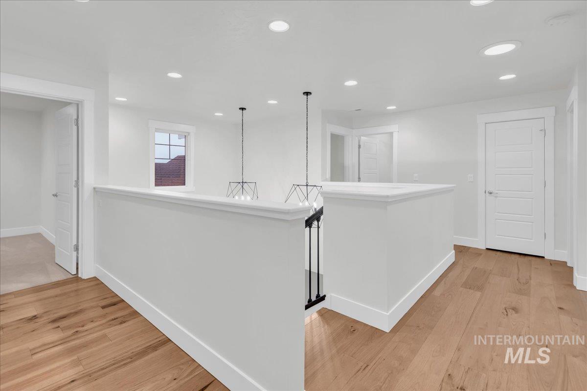 Corridor with an upstairs landing, light wood-style flooring, and recessed lighting