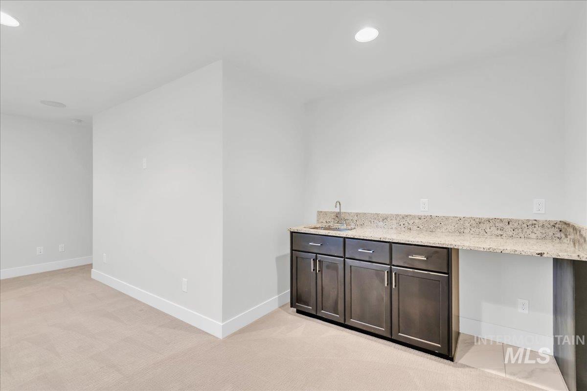 Indoor wet bar with light stone countertops, dark brown cabinetry, light carpet, and recessed lighting