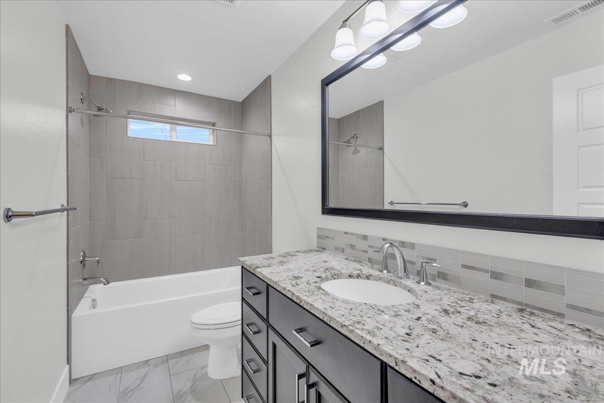 Bathroom with vanity,  shower combination, decorative backsplash, light marble finish flooring, and recessed lighting