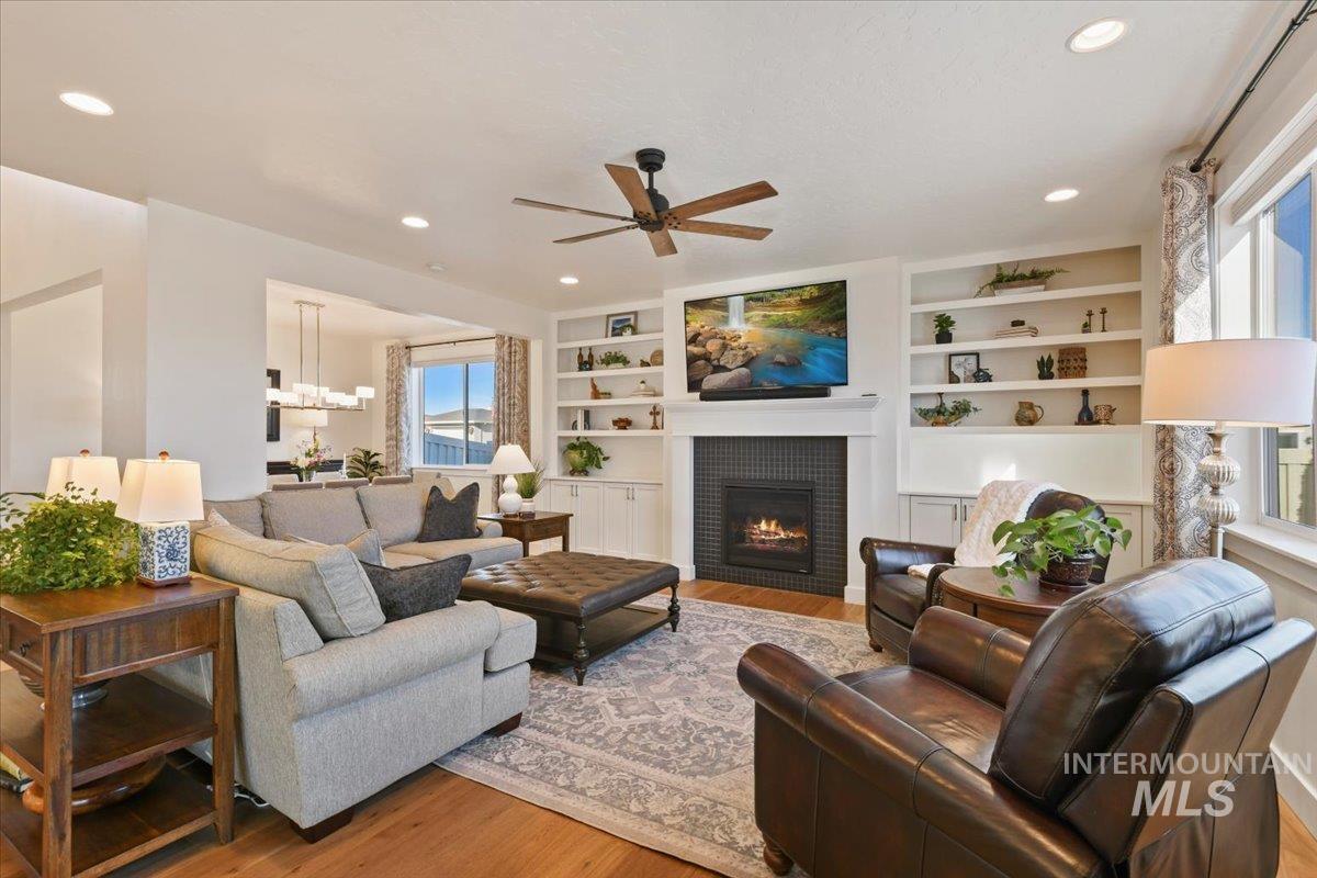 Living room featuring built in shelves, wood finished floors, ceiling fan, a tile fireplace, and recessed lighting