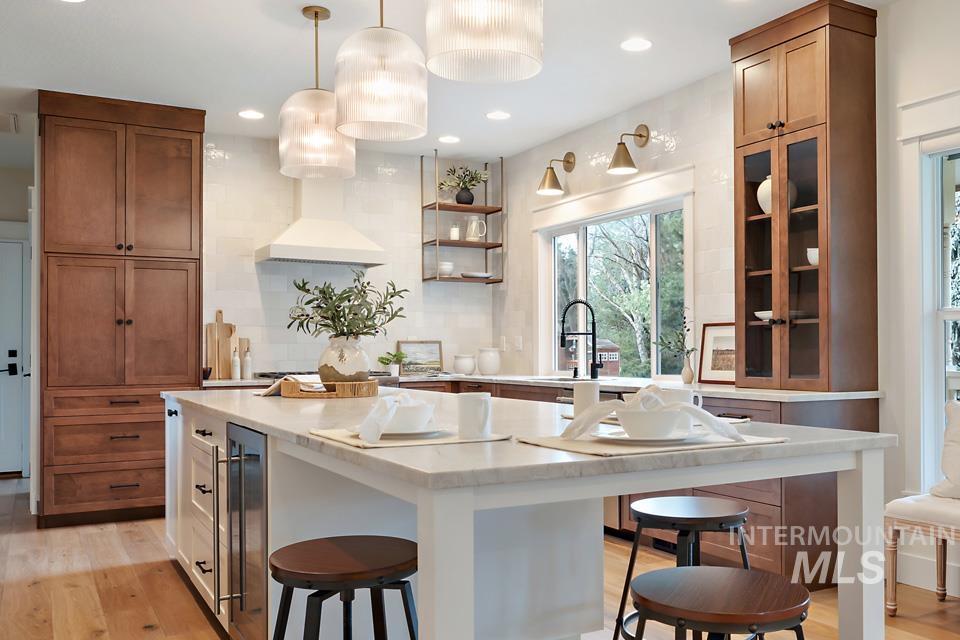 Kitchen with light wood finished floors, brown cabinetry, pendant lighting, light stone countertops, and a kitchen bar