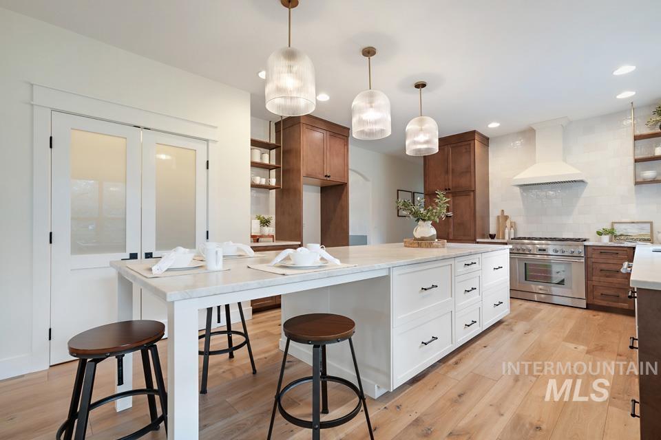 Kitchen featuring open shelves, white cabinetry, high end stainless steel range oven, decorative light fixtures, and custom range hood