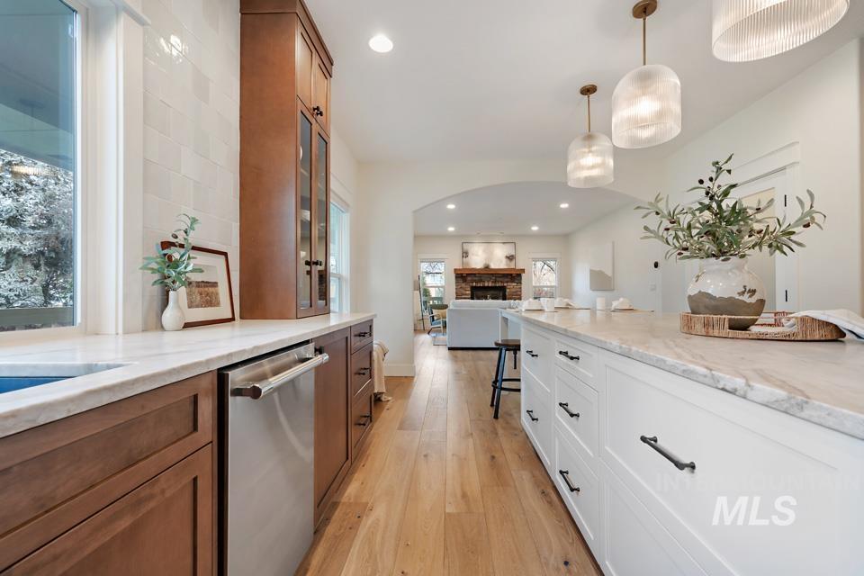 Kitchen featuring brown cabinets, dishwasher, pendant lighting, a fireplace, and light wood finished floors