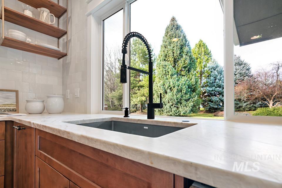 Kitchen with backsplash, light stone countertops, brown cabinets, and open shelves