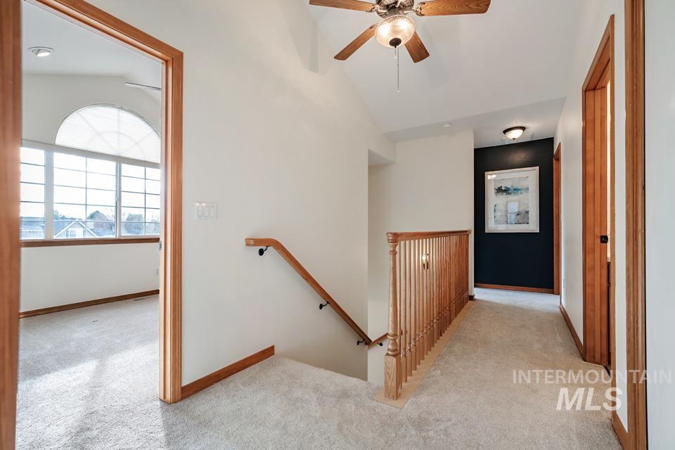 Hallway with an upstairs landing, light carpet, and vaulted ceiling