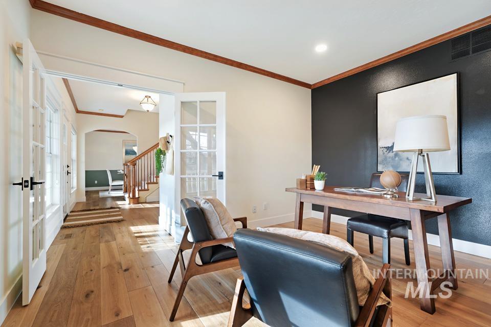 Home office with crown molding, french doors, arched walkways, and light wood-style flooring