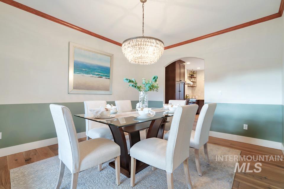 Dining room with arched walkways, ornamental molding, a chandelier, and wood finished floors