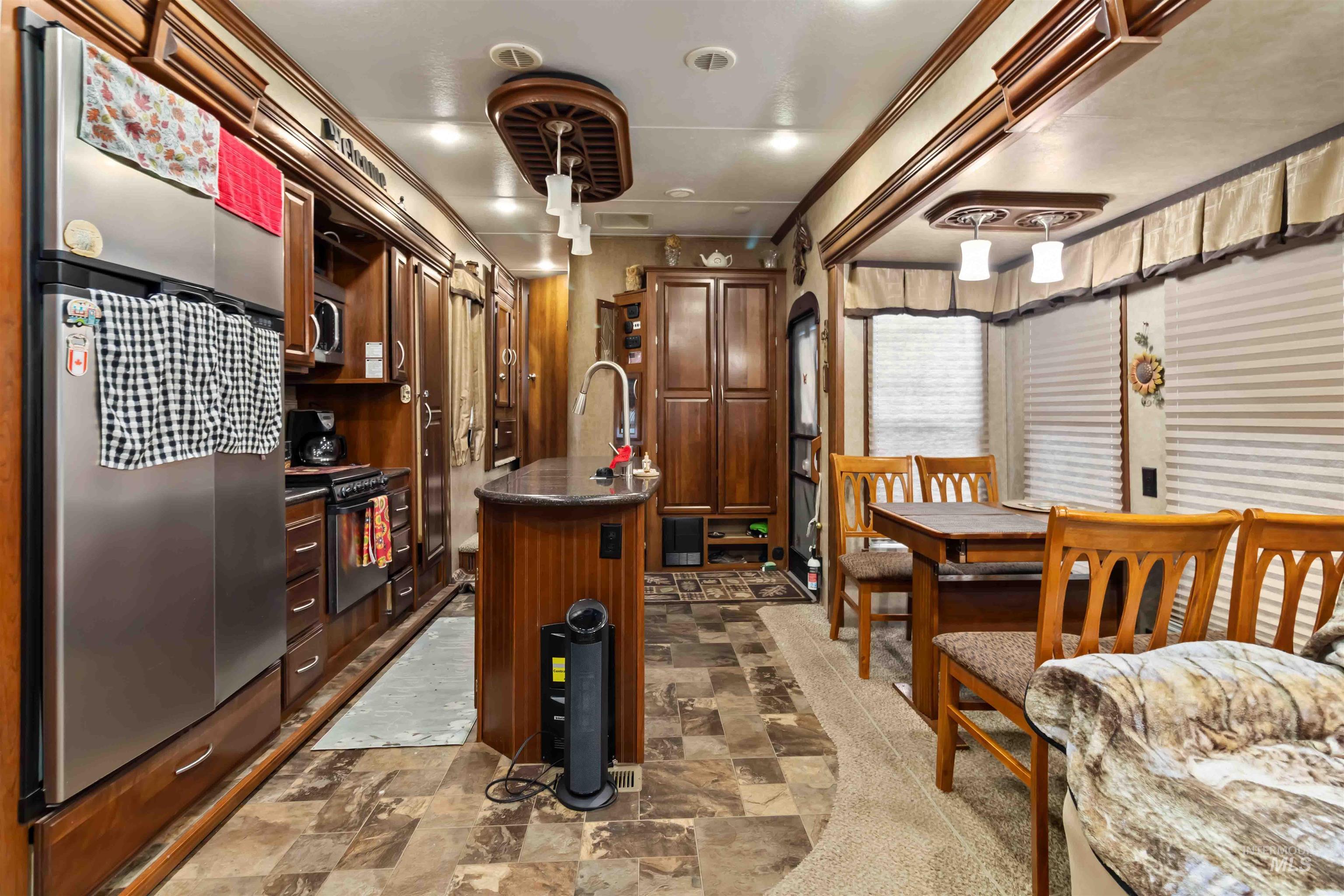 Kitchen with freestanding refrigerator, stone finish floors, a kitchen island with sink, and dark brown cabinets