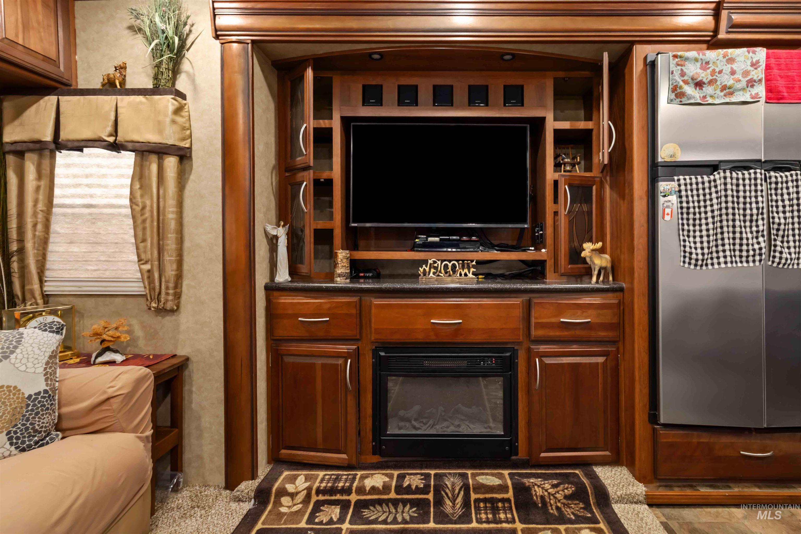 Bar with a fireplace, stainless steel fridge, brown cabinetry, and dark stone countertops