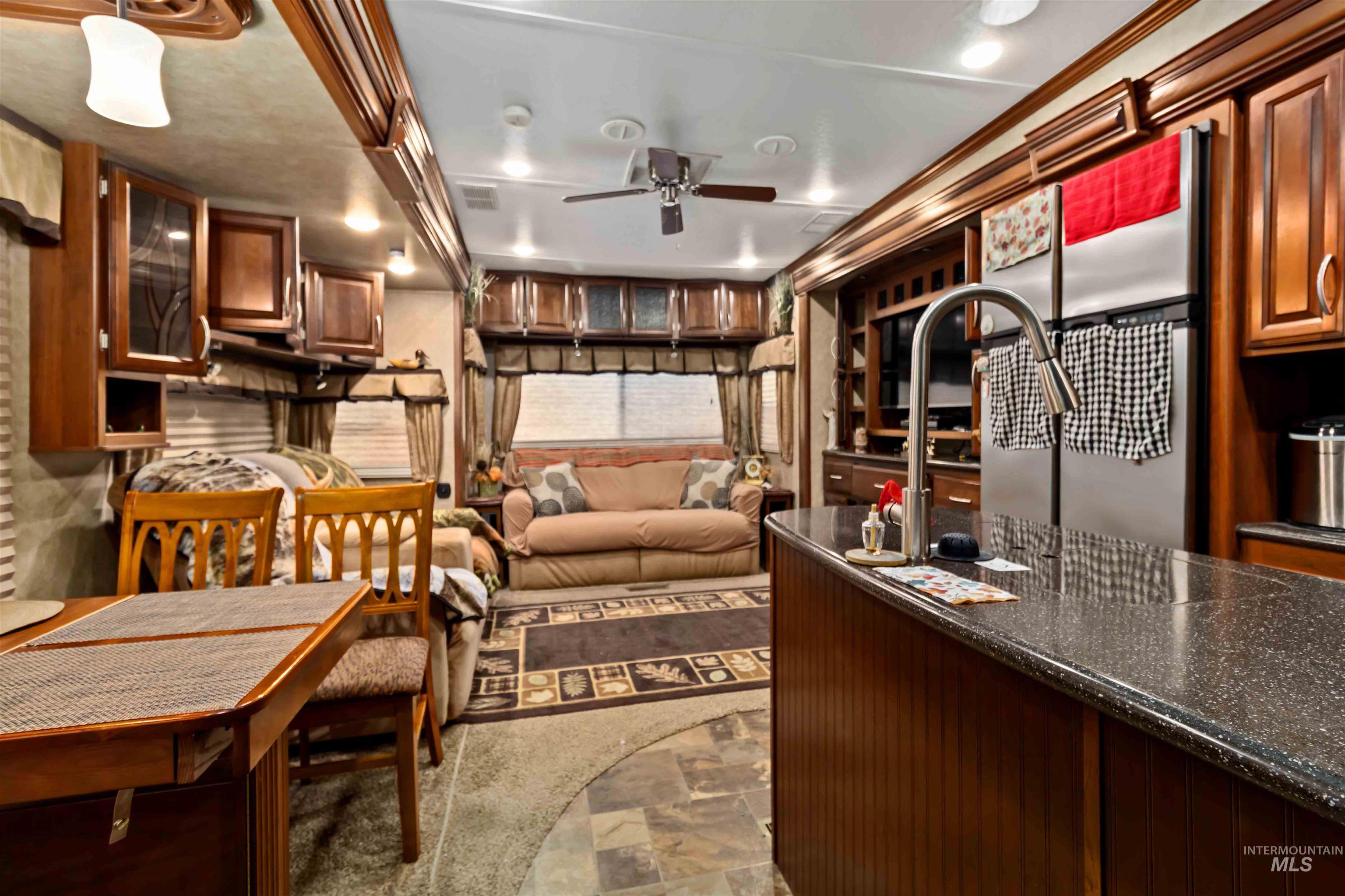 Kitchen featuring dark stone finish flooring, dark stone counters, brown cabinets, ceiling fan, and freestanding refrigerator
