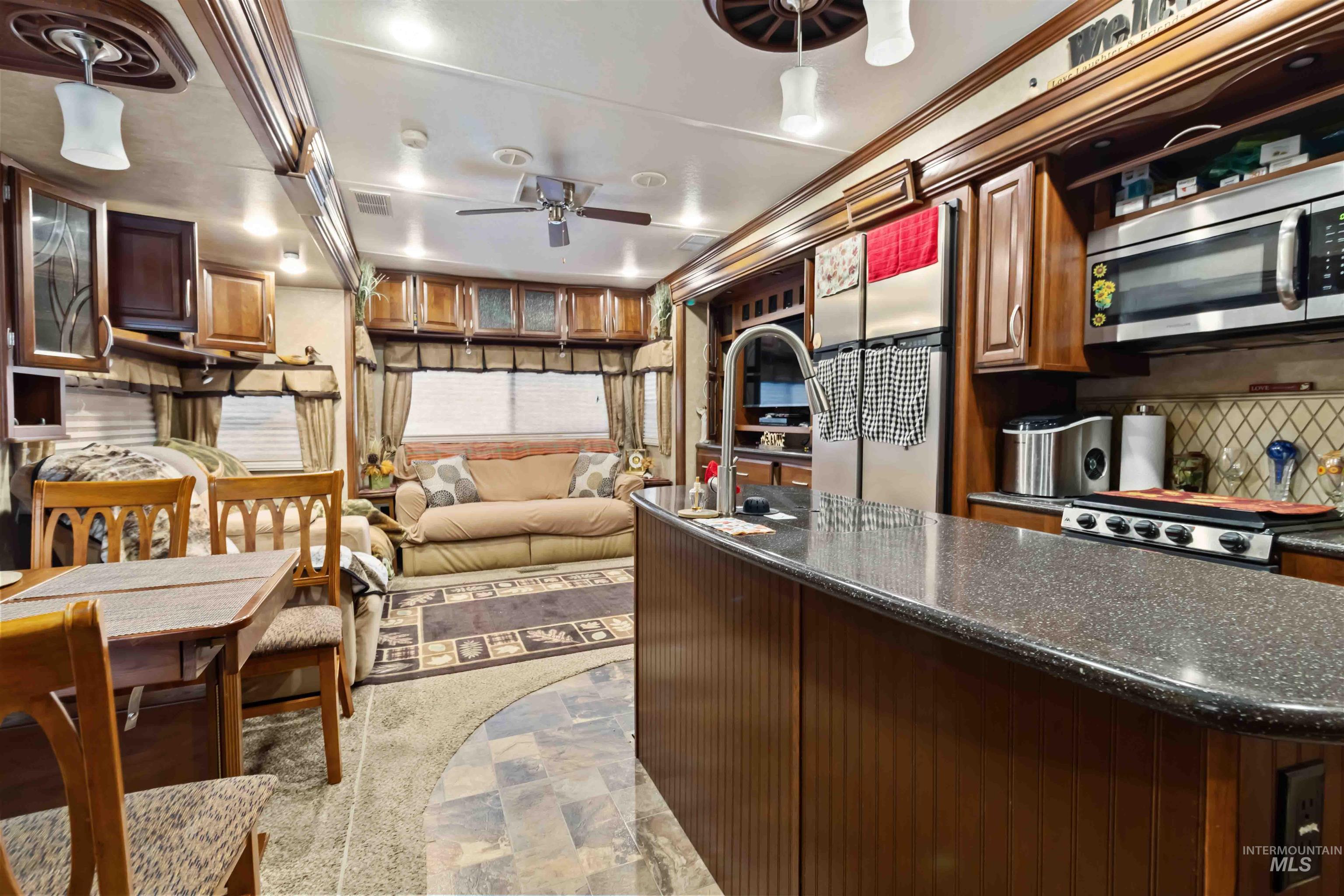 Kitchen featuring stainless steel appliances, dark stone countertops, tasteful backsplash, stone finish floors, and ceiling fan