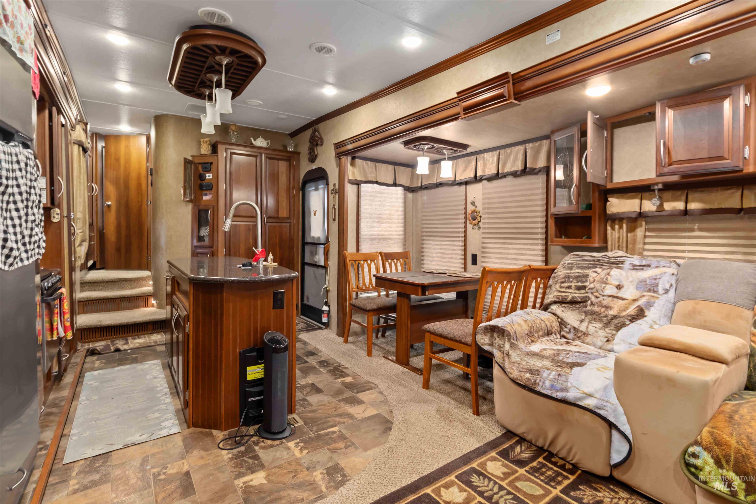 Kitchen with dark countertops, an island with sink, brown cabinetry, crown molding, and stone finish floors