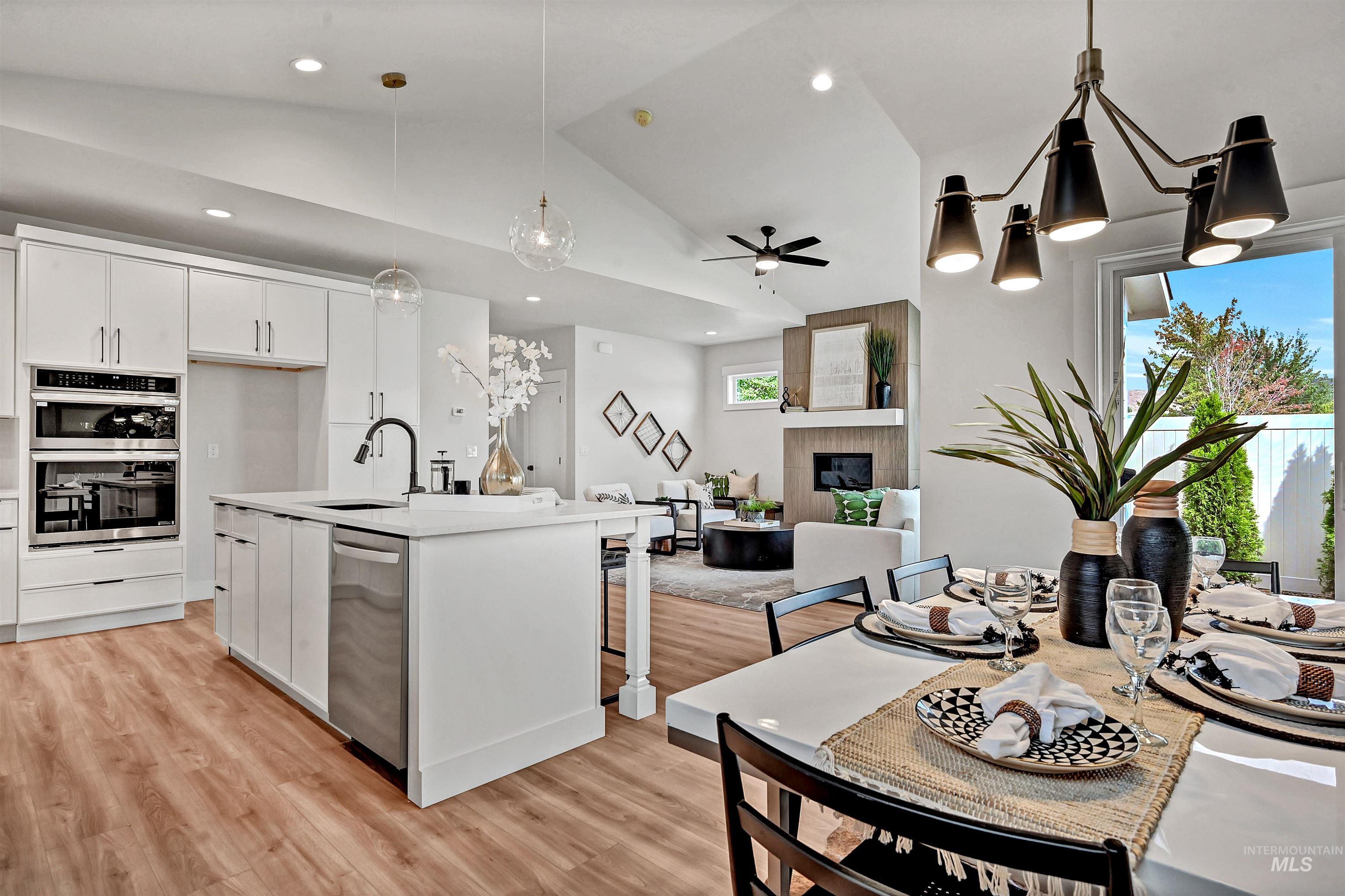 Kitchen featuring pendant lighting, white cabinets, vaulted ceiling, light wood-style flooring, and open floor plan