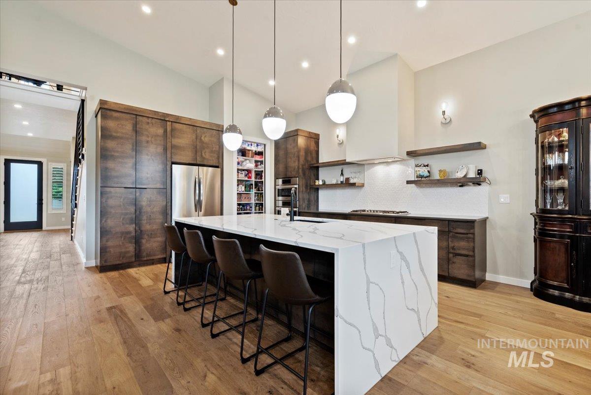 Kitchen with dark brown cabinets, light stone counters, decorative backsplash, a kitchen breakfast bar, and open shelves