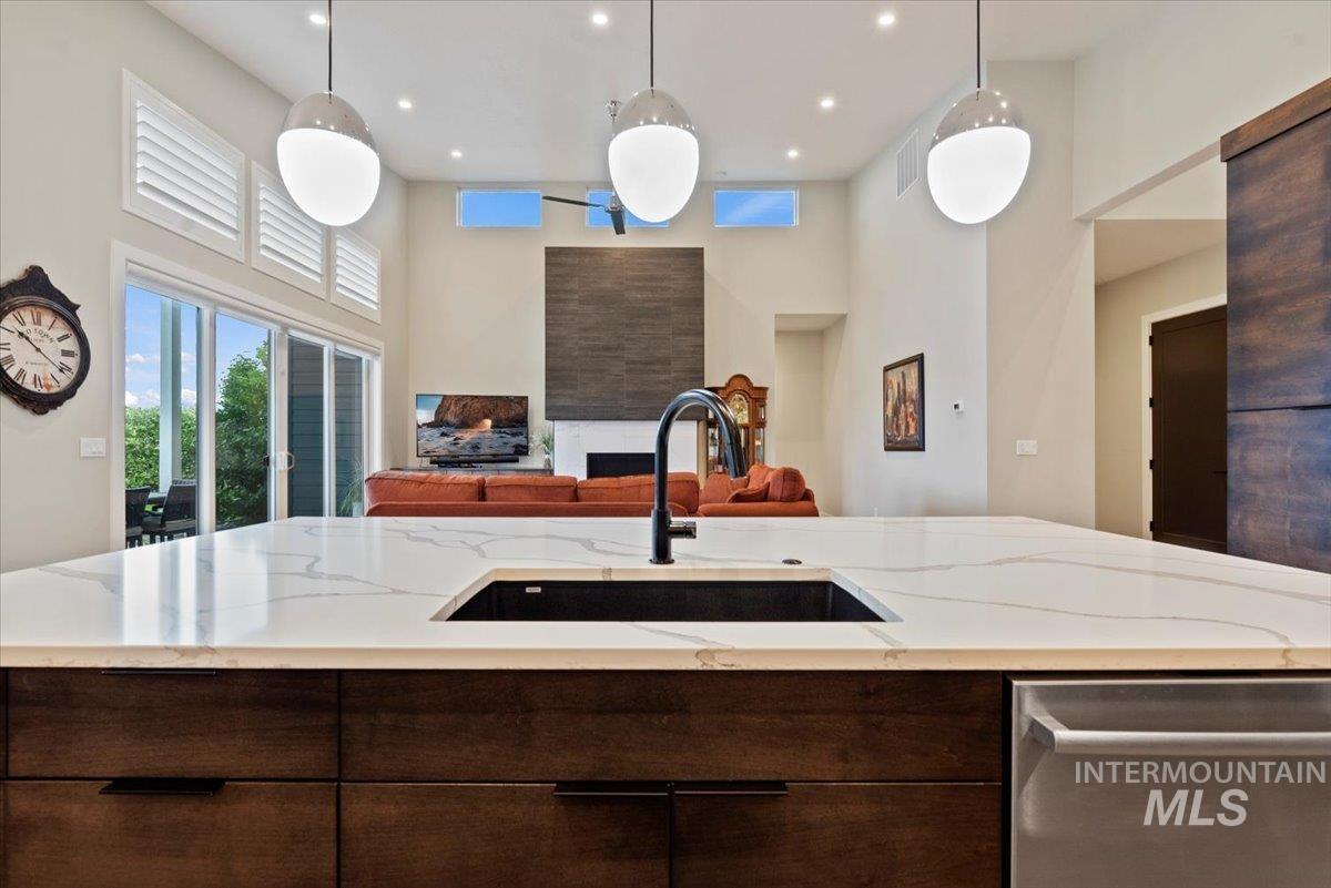 Kitchen featuring dark brown cabinetry, dishwasher, a towering ceiling, hanging light fixtures, and light stone counters