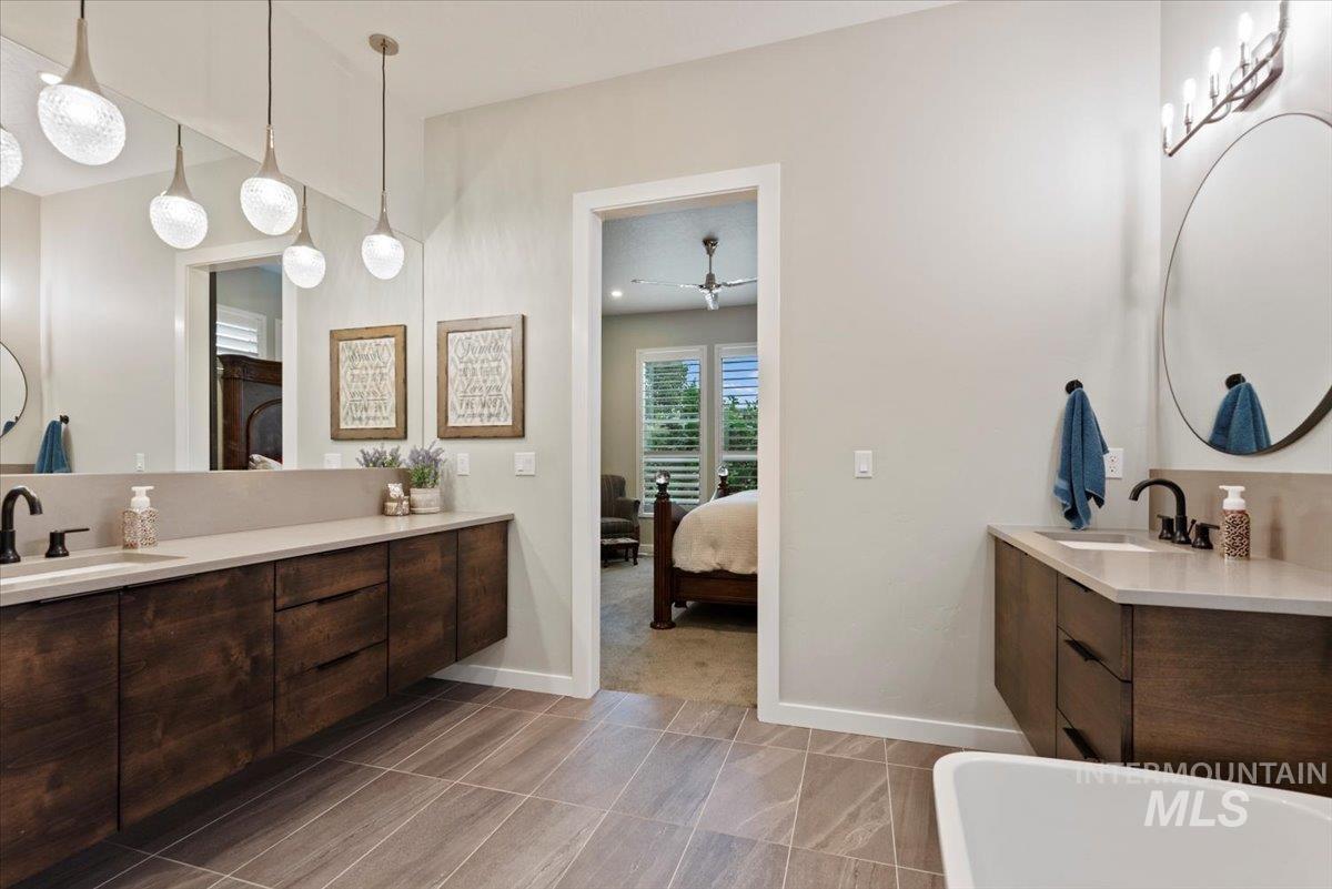 Full bathroom with a freestanding tub, ensuite bath, two vanities, dark tile patterned floors, and a ceiling fan