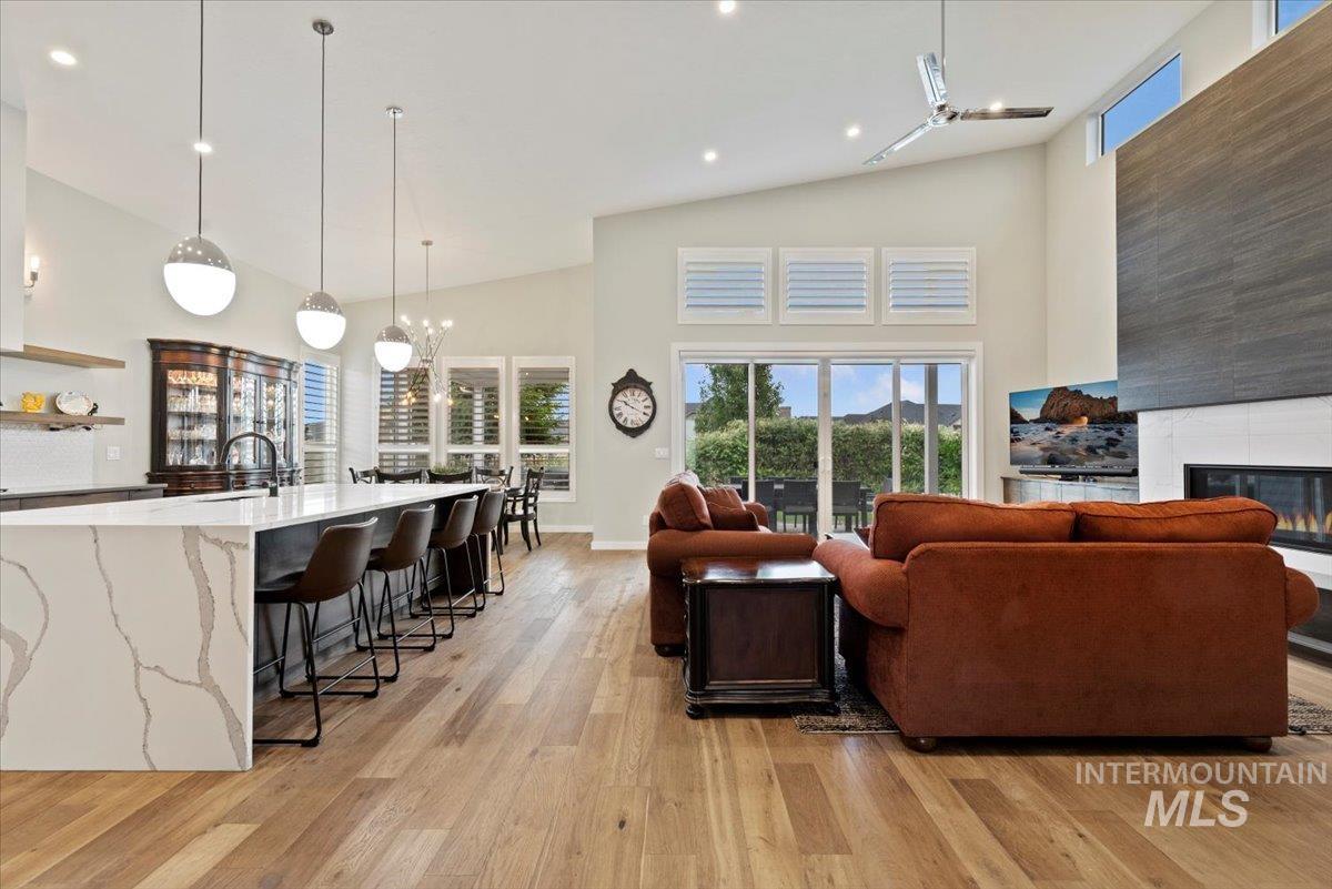 Living room with a fireplace, light wood-type flooring, recessed lighting, and high vaulted ceiling