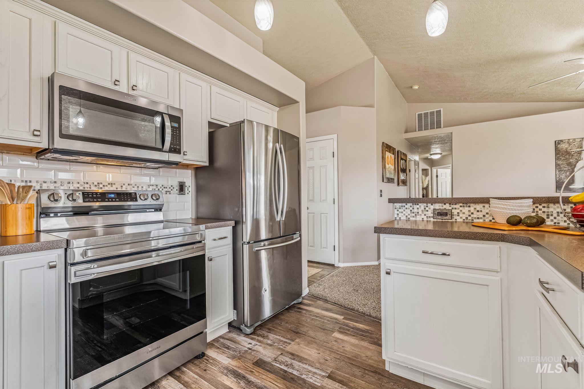 Kitchen with decorative backsplash, appliances with stainless steel finishes, white cabinetry, vaulted ceiling, and dark countertops
